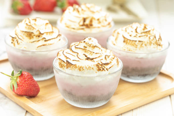 Four individual mini alaska in glass ramekins with strawberry ice cream placed on a brownie, topped with sweet meringue and baked until toasted served on a bamboo tray
