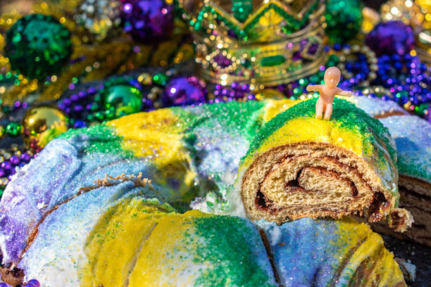 Sliced Mardi Gras King Cake topped with toy baby surrounded by beads and decorations